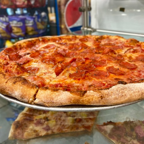 A close-up of a pepperoni pizza on a metal tray, with a crispy crust and melted cheese.