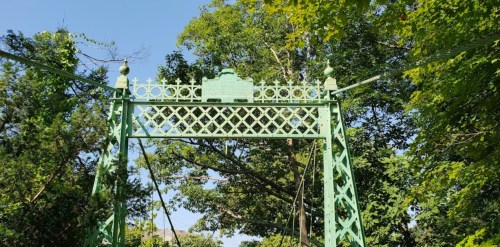 A green decorative bridge structure surrounded by trees under a clear blue sky.
