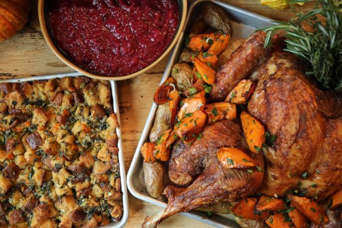 A festive spread featuring roasted turkey with vegetables, stuffing, and cranberry sauce on a wooden table.
