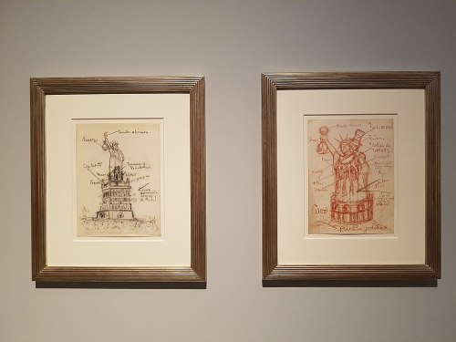 Two framed sketches on a wall, one depicting a tower and the other a statue, both with handwritten notes and annotations.
