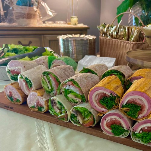 A platter of colorful wraps filled with various meats, vegetables, and greens, arranged neatly on a wooden board.