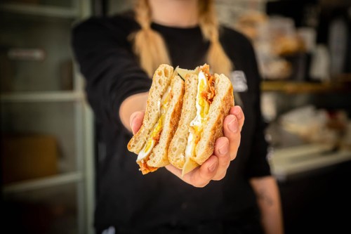 A person holds three stacked sandwiches with eggs, cheese, and bacon, showcasing a delicious breakfast option.