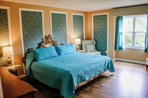 A cozy bedroom featuring a large turquoise bedspread, elegant decor, and natural light from a window.