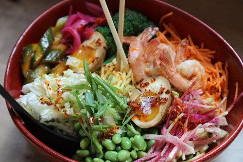A colorful bowl of mixed vegetables, shrimp, and eggs, garnished with herbs and spices, served with chopsticks.