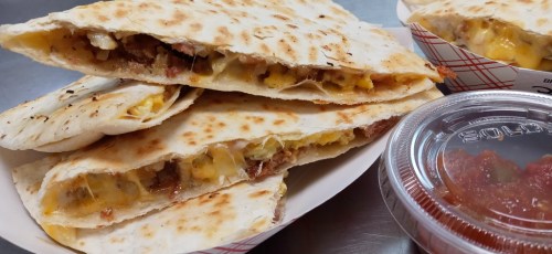 A stack of cheesy quesadillas with meat, served with a side of salsa in a container.