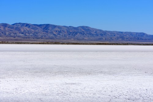 A vast, dry salt flat stretches out under a clear blue sky, with mountains in the background.
