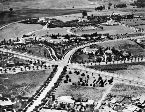 Aerial view of a suburban area with winding roads, houses, and landscaped greenery in a historical black-and-white photo.