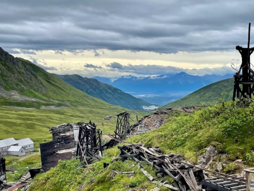 A scenic view of a mountainous landscape with remnants of old structures and lush greenery under a cloudy sky.