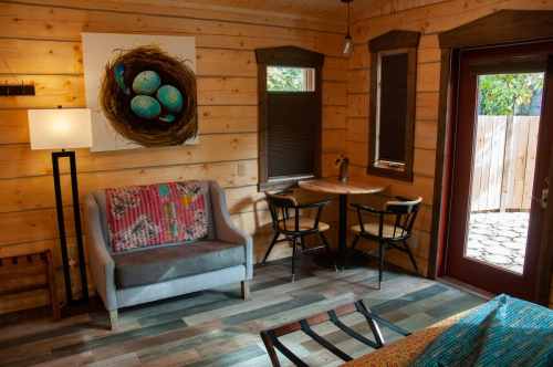 Cozy wooden interior with a sofa, dining table, and artwork of a nest with blue eggs on the wall. Natural light from the door.