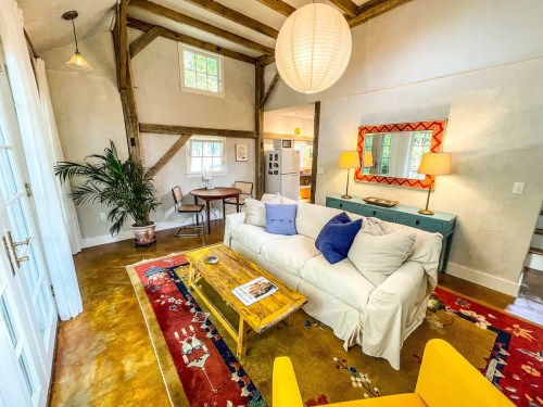 Cozy living room with a white sofa, colorful rug, wooden beams, and a round paper lantern hanging from the ceiling.