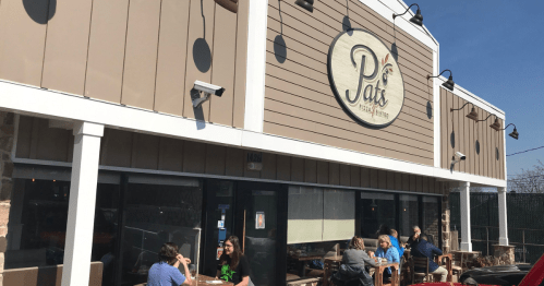 Exterior of Pat's restaurant with outdoor seating, people dining, and a clear blue sky in the background.