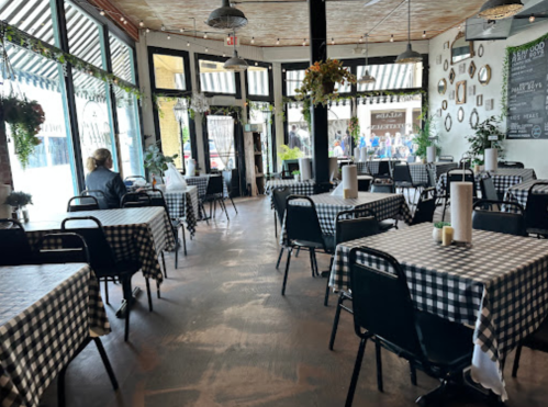 A cozy restaurant interior with checkered tablecloths, plants, and large windows, creating a welcoming atmosphere.