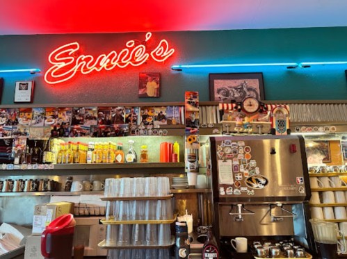 A cozy café interior with a neon sign reading "Ernie's," decorated with photos and various condiments.