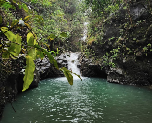 A serene waterfall cascading into a turquoise pool, surrounded by lush greenery and rocky terrain.