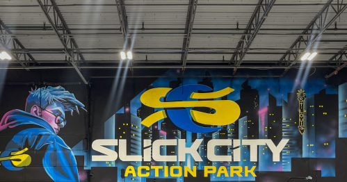 A vibrant mural featuring the logo of Slick City Action Park, with a stylized character and a city skyline backdrop.