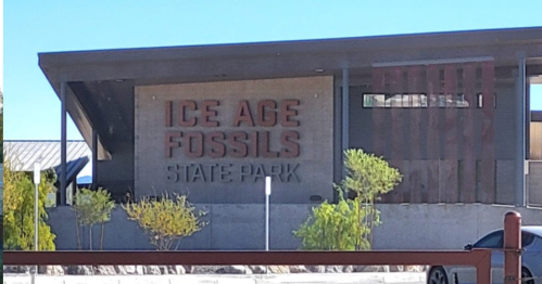 Sign for Ice Age Fossils State Park, featuring modern architecture and greenery in the foreground.