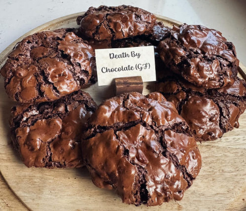 A wooden platter with several chocolate cookies labeled "Death By Chocolate (GF)" in the center.