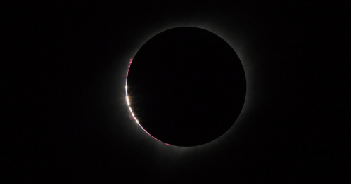 A solar eclipse with a darkened sun surrounded by a glowing corona and bright flares at the edges.