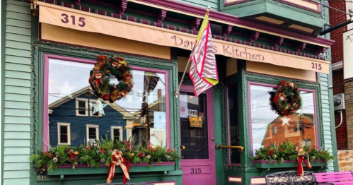 Colorful restaurant exterior decorated with wreaths and festive greenery, featuring large windows and an open sign.