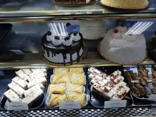 A display case filled with various desserts, including a chocolate cake, pastries, and a coconut cake.