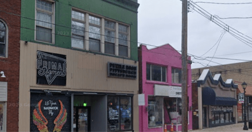A street view featuring colorful storefronts, including a green building and a pink shop, with power lines overhead.