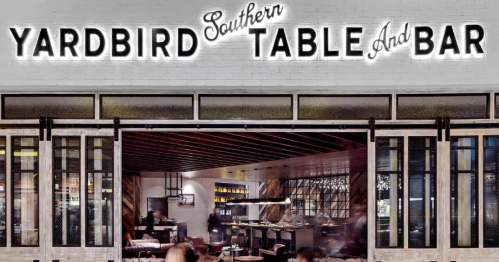 Sign for "Yardbird Southern Table and Bar" with a view of the restaurant's interior and patrons.