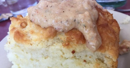 A fluffy biscuit topped with a creamy, seasoned sauce, served on a plate.