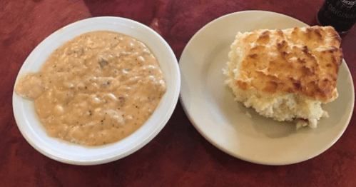 A bowl of creamy chicken gravy with biscuits on a plate, served on a wooden table.