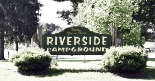 Sign for Riverside Campground surrounded by greenery, inviting visitors to relax and enjoy their stay.