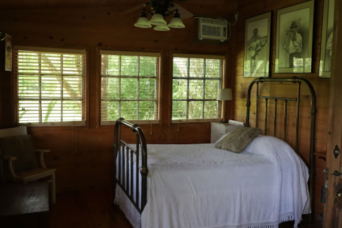 Cozy bedroom with a metal bed frame, white bedding, wooden walls, and large windows letting in natural light.