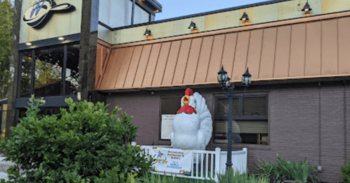 A large chicken statue stands outside a restaurant with a copper roof and decorative lamps.