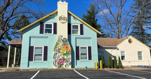 A colorful building with a floral mural, featuring a sign that reads "1881," surrounded by trees and a clear blue sky.
