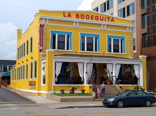 Bright yellow building with blue accents, featuring "La Bodeguita" signage, a restaurant with outdoor seating.