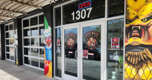 A storefront with large glass doors, featuring colorful clown and monster murals on either side, and an "Open" sign.