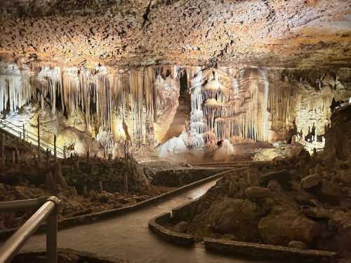 A dimly lit cave interior featuring stalactites and stalagmites, with a winding path and water flowing through.