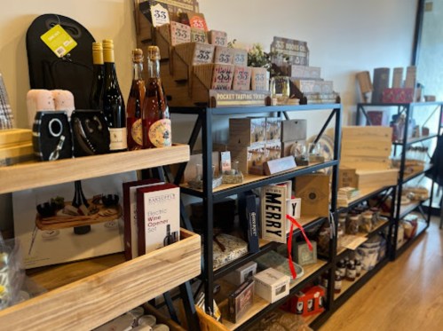 Shelves filled with various gift items, including wine, kitchen gadgets, and decorative boxes in a cozy shop setting.