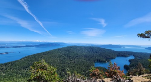 A panoramic view of lush green islands and blue waters under a clear blue sky with wispy clouds.