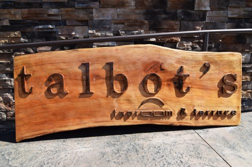Wooden sign with carved text reading "talbot's taproom & terrace" against a stone background.