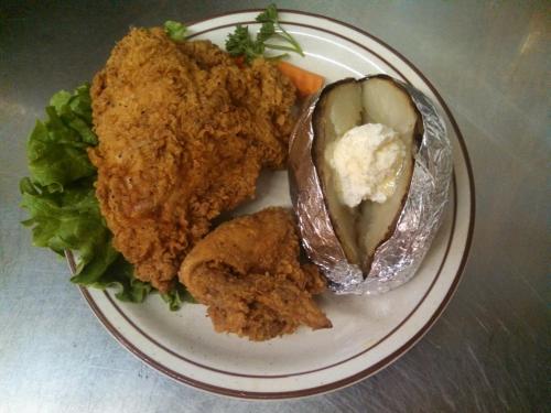 A plate featuring fried chicken, a baked potato with sour cream, and lettuce, garnished with a slice of carrot.