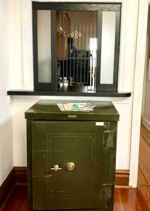 A vintage green safe sits on a wooden floor, with a window and counter visible in the background.