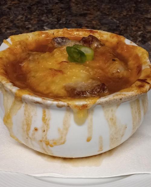 A bowl of cheesy French onion soup, bubbling with melted cheese and garnished with green onions.