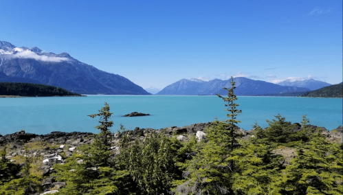A serene landscape featuring turquoise water, rocky shores, and mountains under a clear blue sky.