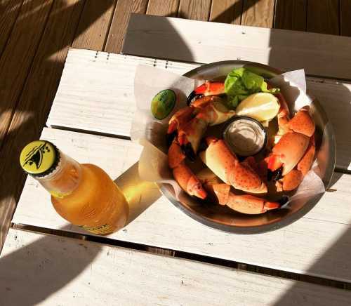 A bowl of crab claws with lemon and lettuce, accompanied by a bottle of beer on a wooden table.