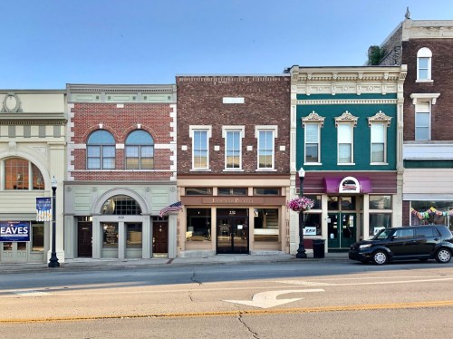 Historic storefronts line a street, featuring brick and colorful facades, with a clear blue sky above.