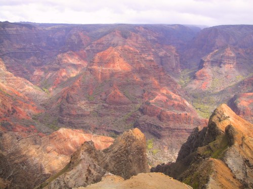 A panoramic view of colorful, rugged mountains and valleys under a cloudy sky.