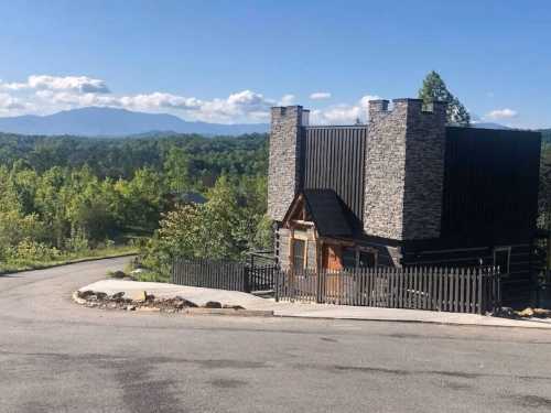 A unique black and stone house on a winding road, surrounded by lush greenery and mountains in the background.