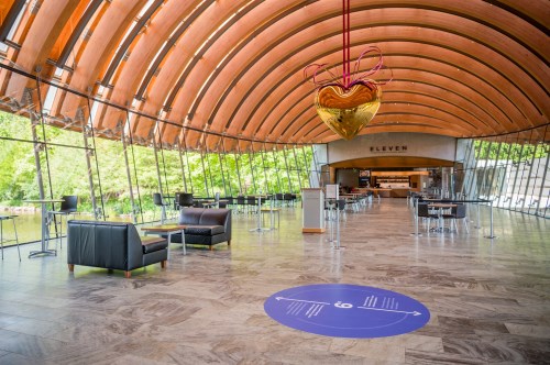 Modern interior of a spacious café with wooden arches, tables, and a large heart-shaped decoration hanging above.