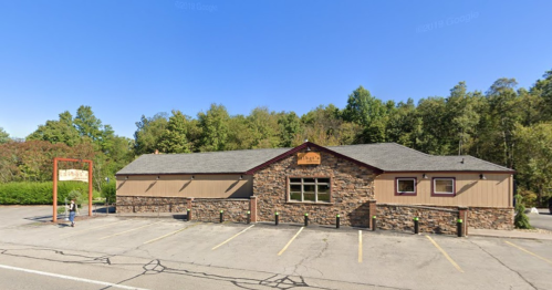 A stone and wood building with a sign, surrounded by trees and a parking lot.
