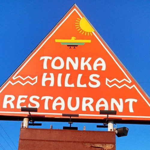 Bright orange triangular sign for "Tonka Hills Restaurant" with a sun and decorative elements.