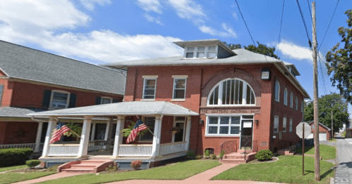 Historic brick building with large windows, porch, and American flags, housing the American National Bank.